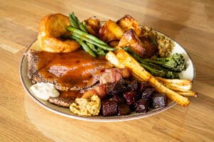 Slices of top rump beef served with beef dripping roast potatoes, diddly squat farm beer mustard, horseradish, cubed beetroot, honey roast parsnips, broccoli, stuffing, green beans and Yorkshire pudding coated in beef gravy