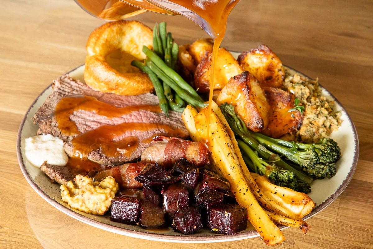 Medium roast top rump beef with crispy roast potatoes and all the sides pouring gravy ready to serve.