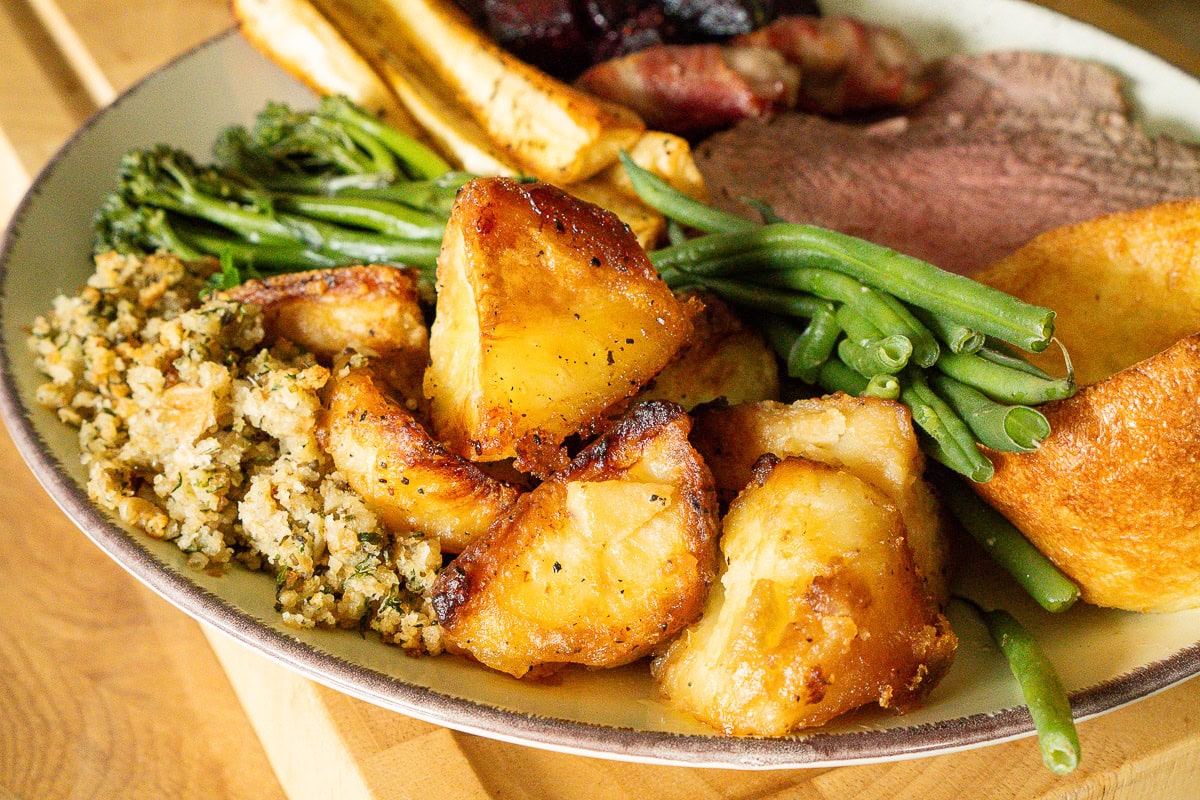 Perfectly cooked roast potatoes on a plate with roast dinner sides and roast beef