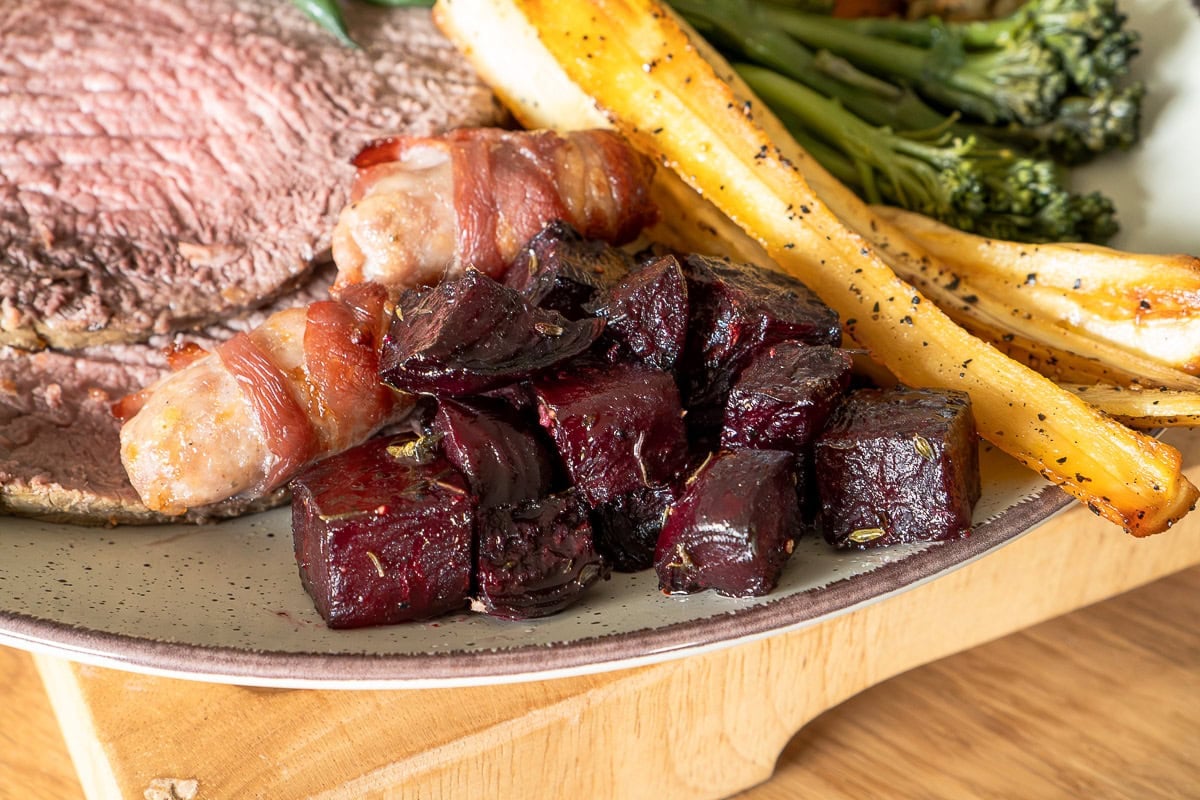 Sliced beef with beetroot cubes and roasted vegetables on plate.