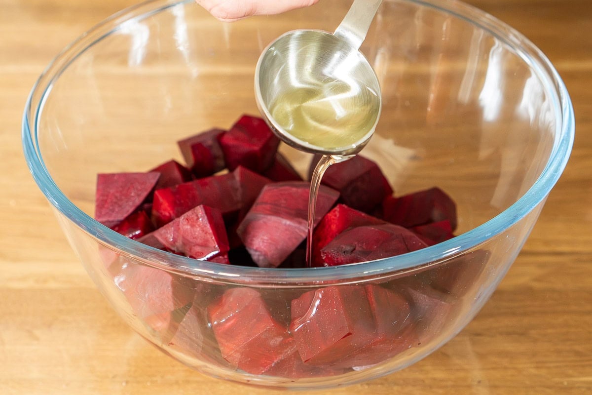 Beetroot cubes being poured with olive oil over a glass bowl.