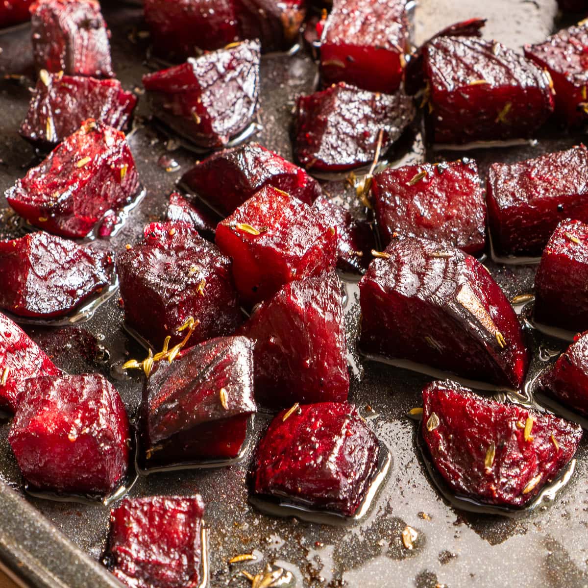 Beetroot cubes roasted on a tray, glossy and deep red with herbs.