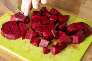 Beetroot cubes being chopped on a green cutting board.